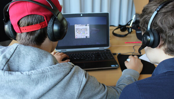 Zwei Jugendliche sitzen vor einem Laptop und spielen.