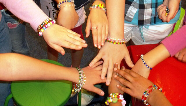 Viele Kinder halten ihre mit unterschiedlichen Armbändern verzierten Hände aufeinander in die Mitte eines Kreises.