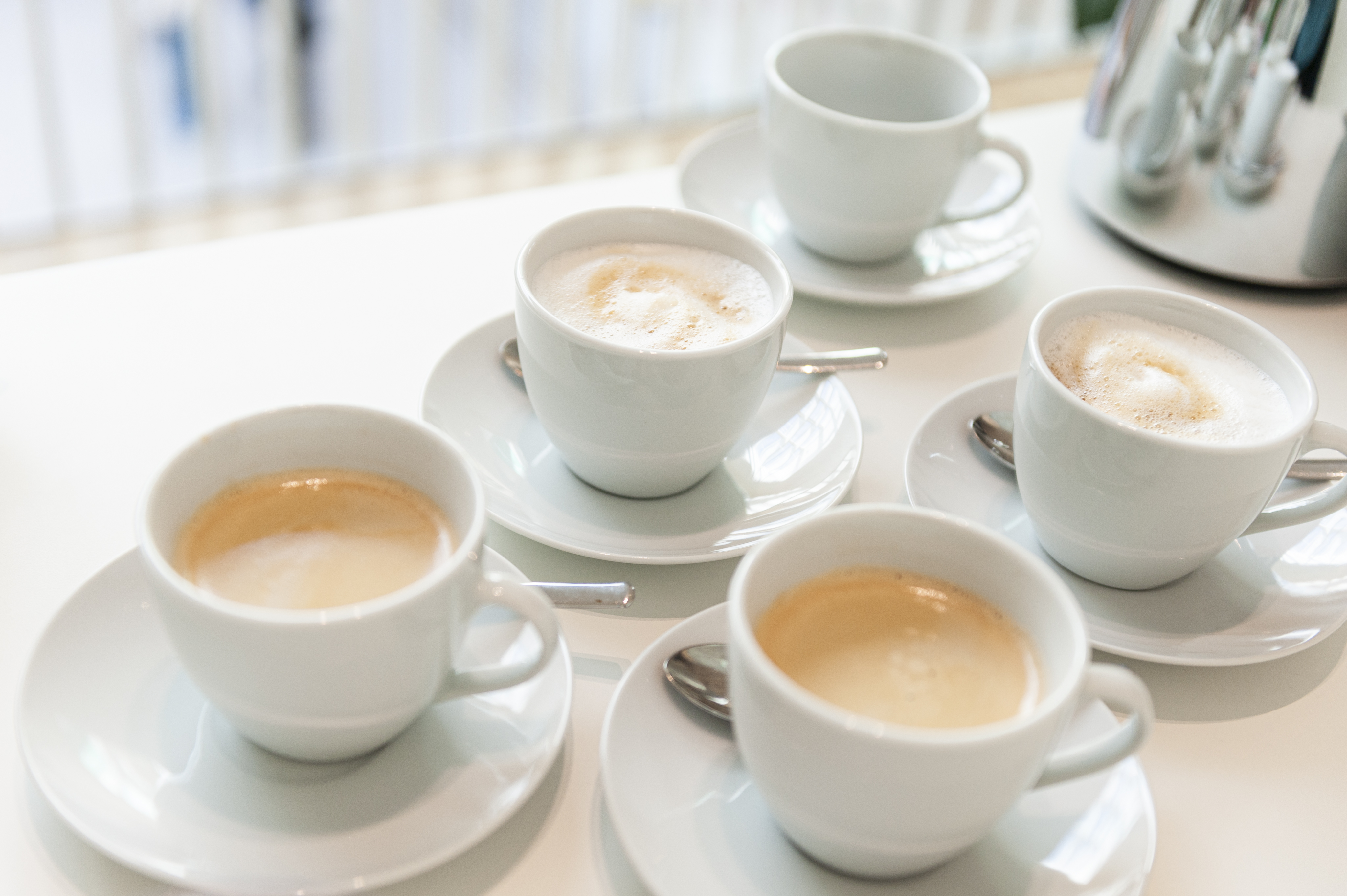 Vier volle Tassen Kaffee und eine leere auf einem Tisch.